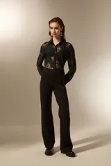 Pantalón tipo calza flare de tiro alto, color negro, con detalle de tachas metálicas plateadas a lo largo de las costuras laterales.