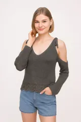 Sweater de algodón tejido, color gris oscuro, con diseño de hombros descubiertos, escote en V profundo y detalle de lazos anudados en los hombros. Presenta un borde inferior con terminación ondulada y mangas largas.