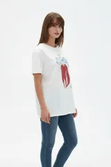 Remera de algodón color beige con estampado frontal de un corazón rosado que contiene un moño. Tiene cuello redondo y mangas cortas.