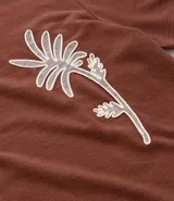 Remera marrón de corte regular, cuello redondo y manga corta, con estampa bordada de una palmera en el frente.