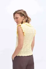 Chaleco tejido de punto color amarillo, con diseño calado, escote redondo y volados en los hombros y cuello. Cuenta con cierre frontal de botones forrados al tono.
