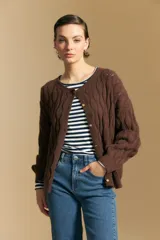 Cardigan de punto color terracota con diseño de trenzas verticales, cuello redondo y cierre frontal con botones metálicos. Presenta mangas largas con puños ajustados y un calce holgado.