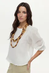 Blusa de lino blanca con escote redondo y mangas cortas abullonadas con detalles de volados en los puños.