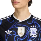 Camiseta de fútbol Adidas de la Selección Argentina, modelo visitante. Diseño en color negro con estampado de patrones florales y ornamentales en tonos azules, cuello redondo blanco y detalles de las tres tiras en los hombros. Incluye el escudo de la AFA, el logo de Adidas y el parche de campeón del mundo FIFA 2022.