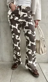 Pantalón de jean de corte recto con estampado de manchas de vaca en tonos marrón y blanco.