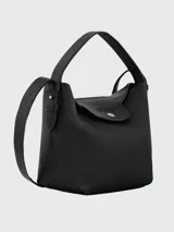 Cartera bucket S Longchamp modelo Le Cadence, color negro, confeccionada en cuero graneado. Cuenta con un asa superior fija, solapa frontal con botón a presión dorado y una correa ajustable para llevar al hombro o cruzada.