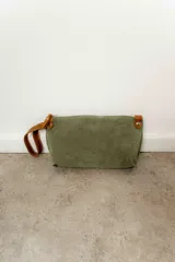 Sobre de mano color verde oliva, confeccionado en cuero gamuzado, con cierre superior y tira de cuero marrón en el lateral.