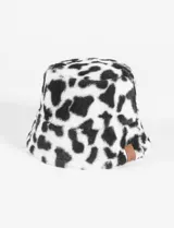 Gorro tipo bucket de pelo sintético con estampado de manchas de vaca en blanco y negro. Presenta una etiqueta pequeña de cuero sintético en el lateral.