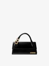 Bolso estructurado de cuero liso color negro, con asa superior reforzada, detalle de hebilla metálica dorada y logo de la marca en letras doradas en la parte frontal.