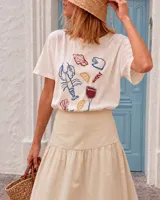 Remera de silueta amplia y calce relajado, confeccionada en tela suave y liviana de color blanco. Presenta cuello redondo, mangas cortas con hombros caídos y estampa gráfica multicolor en el frente con motivos variados.