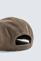 Gorra de cinco paneles confeccionada en pana de algodón, con visor plano y ajuste posterior. Presenta un bordado frontal con el texto 'Lassen Field'.