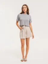 Short color beige de lino con tiro alto, elástico en la pretina trasera, cierre delantero con botón, tablas en el frente, bolsillos delanteros y dobladillo invisible.