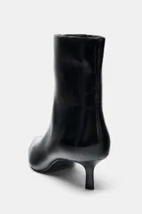Botín de tacón kitten en acabado charol negro, con diseño de punta fina y cierre lateral mediante cremallera.