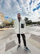 Campera de hombre color crema, de textura peluda, con cierre frontal, cuello alto, bolsillos laterales y un bolsillo impermeable negro en el pecho.