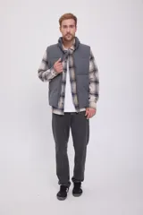 Chaleco puffer gris sin mangas con cuello alto y cierre de cremallera. Tiene bolsillos frontales y relleno de fibra sintética.