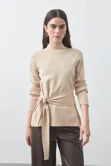 Polera de tejido de punto color beige, con cuello alto, manga larga y detalle de lazo ajustable en la cintura que aporta estructura a la silueta.