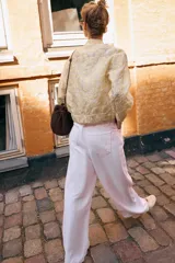 Chaqueta tipo bomber de cuello redondo y manga larga, confeccionada en tejido jacquard con diseño floral en tonos dorados y crema. Presenta cierre frontal con cremallera, bolsillos delanteros de plastrón con solapa y puños y bajo elásticos.