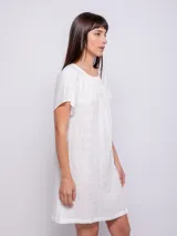 Vestido corto de corte holgado, color celeste, con cuello redondo fruncido y mangas cortas. Está confeccionado en una tela con textura diferenciada que le aporta relieve.