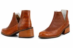 Botín de cuero blanco con textura de crocco y charol, diseño con calados circulares y aberturas laterales en forma de V. Cuenta con taco foliado de madera y vira cosida.