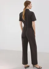 Enterito largo de algodón estilo tejano, color marrón, con cuello camisero, mangas cortas, cierre frontal con cremallera y cinturón ajustable en la cintura.