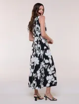 Vestido maxi sin mangas de seda fría, color negro con estampado floral blanco y verde. Presenta escote cruzado con detalle de abertura y corte en la cintura con falda amplia.