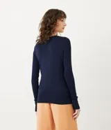 Suéter de punto color rosado, con cuello barco, mangas largas y puños con botones decorativos. El dobladillo también es acanalado.