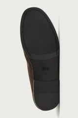 Mocasines de vestir para hombre confeccionados en piel con acabado en gamuza de color marrón, con detalle de borlas en el empeine y suela plana con ligero tacón.