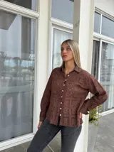 Camisa de manga larga en color marrón, confeccionada en tela con diseño calado geométrico. Presenta cuello clásico, cierre frontal con botones y puños abotonados.