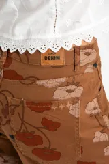 Jean de corte baggy y tiro medio, confeccionado en algodón peinado. Presenta un diseño estampado con motivos florales en tonos tierra sobre una base color marrón.