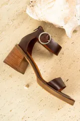 Sandalias de cuero color marrón con tira ancha sobre los dedos y tira con hebilla al tobillo. Tacón de madera.