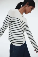 Saco corto de punto fino suave, color blanco con rayas horizontales negras. Presenta escote redondo, botones frontales y remate acanalado en puños y bajo.