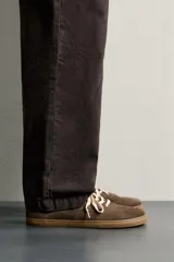Zapatilla deportiva barefoot fabricada en piel con acabado serraje de color marrón, con cordones en contraste y suela fina de goma.