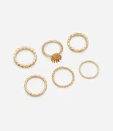 Set de seis anillos de metal dorado con diferentes texturas y diseños, incluyendo un modelo con detalle central en forma de flor.