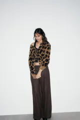 Chaqueta de punto con textura suave, cuello redondo y manga larga. Presenta un diseño de estampado animal print en tonos marrones y negros, con cierre frontal de botones.