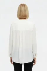 Blusa blanca de viscosa con detalles de broderie en los hombros, cuello en V y mangas largas holgadas.