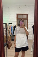 Remera blanca de manga corta y corte holgado con un estampado frontal que incluye una botella de vino, una copa de vino y la palabra "VINO" escrita al revés.