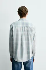 Camisa de algodón con efecto lavado, diseño a cuadros en tonos celestes y beige, cuello solapa, manga larga con puños abotonados y bolsillos frontales con solapa.