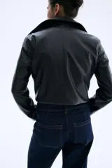 Jean de tiro alto en denim azul oscuro con pierna amplia y corte tobillero. Presenta un diseño de cinco bolsillos, cierre frontal con botón y costuras decorativas verticales en el frente que simulan un pliegue.