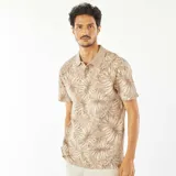 Remera tipo polo color beige con estampado de hojas en tonos marrones y blancos.