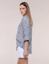 Blusa de silueta relajada con textura tramada, color azul con rayas verticales en tonos rosados, celestes y amarillos. Cuenta con cuello mao abierto en V y mangas tres cuartos amplias con pequeña abertura lateral en el puño.