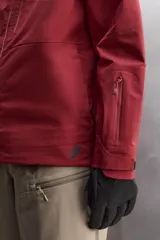 Cazadora deportiva de esquí con diseño bicolor en tonos negro y verde oliva. Presenta capucha amplia con visera, cierre frontal con cremallera termosellada, bolsillos frontales y en manga con cierres impermeables, y aberturas de ventilación en las axilas. Incluye faldón interior antinieve, puños ajustables y tecnología de rescate RECCO.