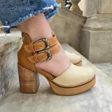 Zapatos de tacón alto con plataforma, confeccionados en cuero color marfil y marrón tostado, con taco ancho de madera y doble tira con hebillas metálicas ornamentadas en el empeine.