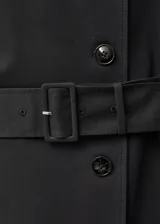Trench coat largo de color negro con diseño de doble botonadura, cuello con solapa, trabillas en hombros y puños, y cinturón desmontable con hebilla. Cuenta con forro interior y abertura posterior.