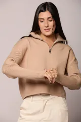 Buzo tejido de punto color beige, con cuello alto y cierre frontal parcial. Presenta mangas largas con diseño en tejido morley y corte holgado.
