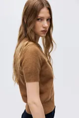 Sweater de punto suave con ajuste entallado, cuello redondo y mangas cortas. Presenta terminaciones acanaladas en cuello, puños y bajo.