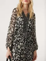 Vestido largo de gasa color negro con estampado floral blanco, escote en V cruzado, mangas largas con aberturas en los hombros y falda con volantes.