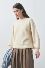 Sweater de tejido liviano con silueta relajada, hombros caídos y mangas largas con puños ajustados. Presenta cuello redondo y lazos ajustables en el bajo.