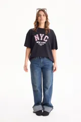 Remera de algodón negra de manga corta y corte holgado, con estampa frontal con la inscripción "NYC New York The Big Apple City".