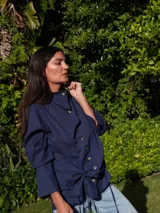 Camisa negra de lino con cuello camisero, abotonada al frente y mangas largas con puños abotonados. Tiene un sistema de ajuste con cordones en la parte delantera que permite usarla larga o fruncida.