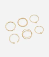 Kit de seis anillos de metal con acabado dorado claro. El conjunto presenta diversos diseños minimalistas y orgánicos, incluyendo un anillo con textura de cuentas, uno de forma ondulada, uno abierto con esferas en las puntas, uno con un pequeño dije circular, uno con un nudo y uno de doble aro entrelazado.